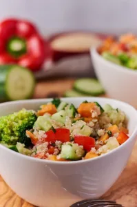 Ein weißes Schälchen mit einem Salat aus Quinoa, Gemüse und Zitronen-Dressing, der mit Petersilie bestreut wird.